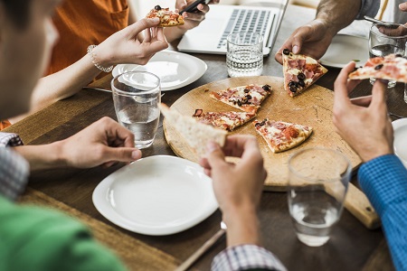 A close-up of coworkers sharing a pizza in a meeting.